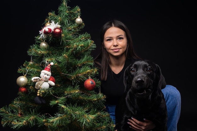 Retrato de un perro Labrador Retriever con su dueño cerca del árbol verde de año nuevo