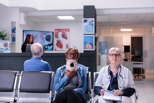 Retrato de una persona con cuello ortopédico sentado en la sala de espera de la clínica consultando con un médico de alto nivel. Mujer usando espuma cervical después de una lesión por accidente hablando con un médico sobre atención médica.