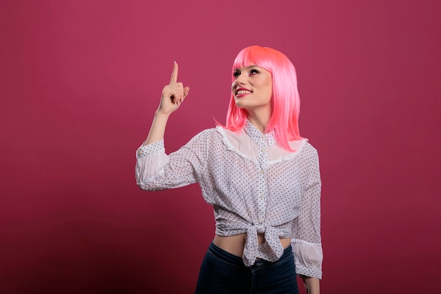 Retrato de una persona hermosa con cabello rosado usando el dedo índice para señalar hacia arriba, indicando direcciones hacia arriba frente a la cámara. Recomendando y señalando arriba y arriba, publicidad.