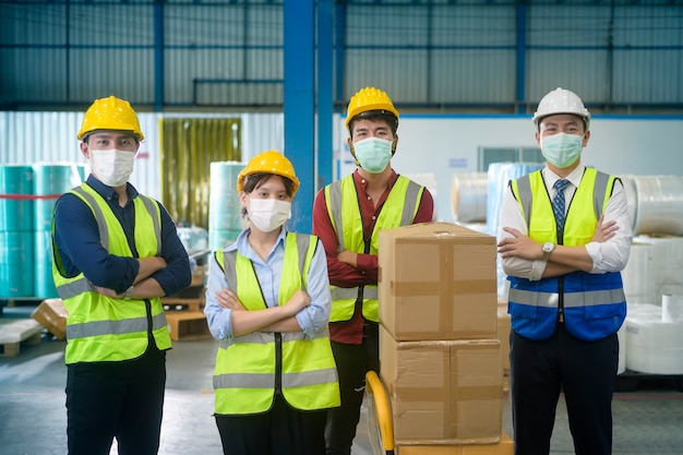 Retrato de personas de ingeniería con máscara médica, casco protector que trabaja en la fábrica de almacén