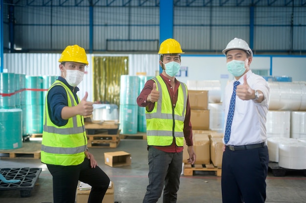 Retrato de personas de ingeniería con máscara médica, casco protector que trabaja en la fábrica de almacén