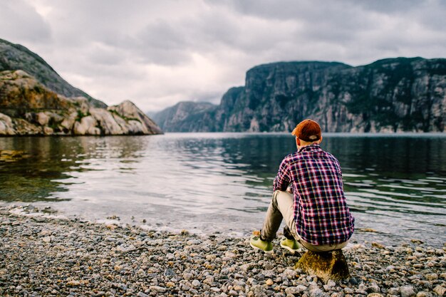 Retrato por trás do homem viajante sentado na pedra no fiorde na noruega e apreciando a paisagem fabulosa natureza.