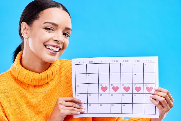 Retrato positivo e mulher com um calendário em um estúdio para rastrear seu ciclo menstrual ou de ovulação Sorriso feliz e rosto de uma modelo feminina com um gráfico de período de papel isolado por um fundo azul