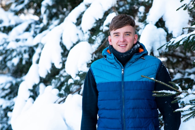 Retrato de positivo feliz joven de pie al aire libre en un bosque nevado de invierno