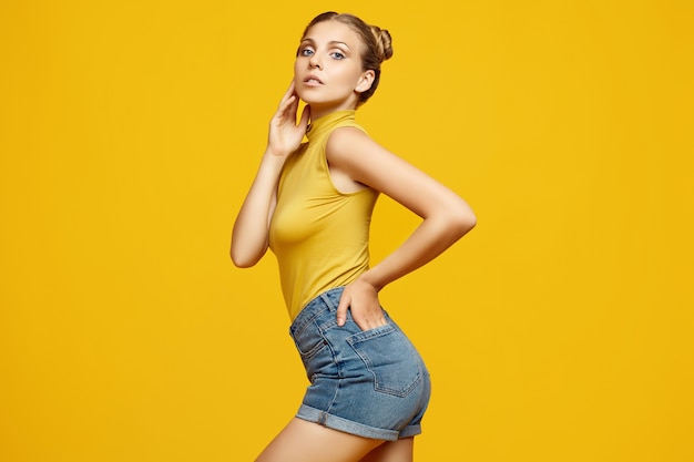 Foto retrato positivo de la hermosa modelo de mujer rubia hipster con pelo rizado posando sobre fondo amarillo colorido en estudio