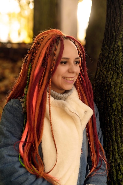 retrato, de, positivo, mujer joven, con, dreadlocks, en, bosque, parque, bastante, hembra, con, brillante, peinado, el mirar lejos, sonriente