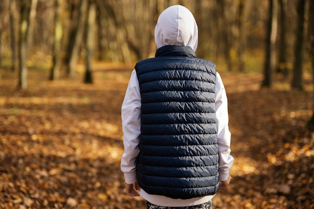 Retrato posterior de un adolescente con capucha y chaleco sin mangas en el bosque de otoño