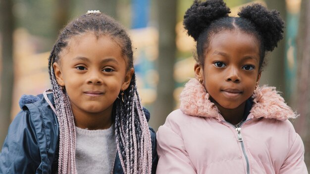 Retrato preadolescente niños lindos primer plano dos hermanas pasan tiempo en el parque de la ciudad amiguitos mirando a la cámara felizmente sonriendo niñas pequeñas sentadas en un banco al aire libre infancia descuidada vacaciones alegres