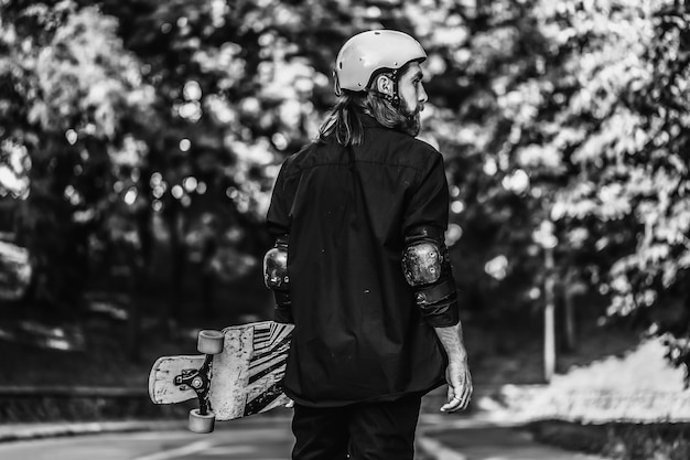 Retrato preto e branco de um cara barbudo segurando um skate, longboard. Foto de alta qualidade