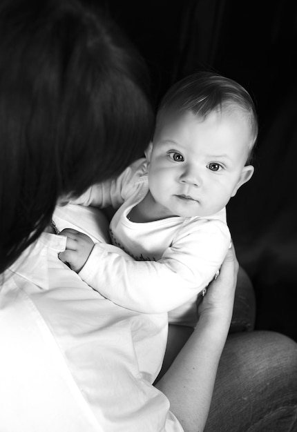 Retrato preto e branco do topo de uma mãe com uma filha de um ano Uma mãe segura uma criança em pé olhando com espanto os braços da criança no peito