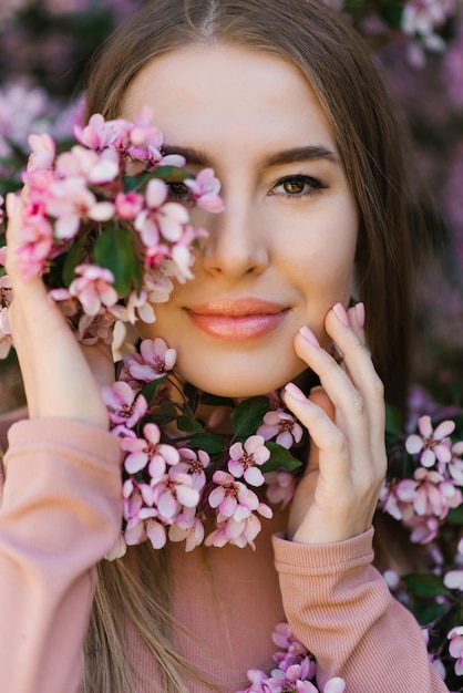 Retrato de primavera de una hermosa niña bajo un manzano floreciente con flores rosas