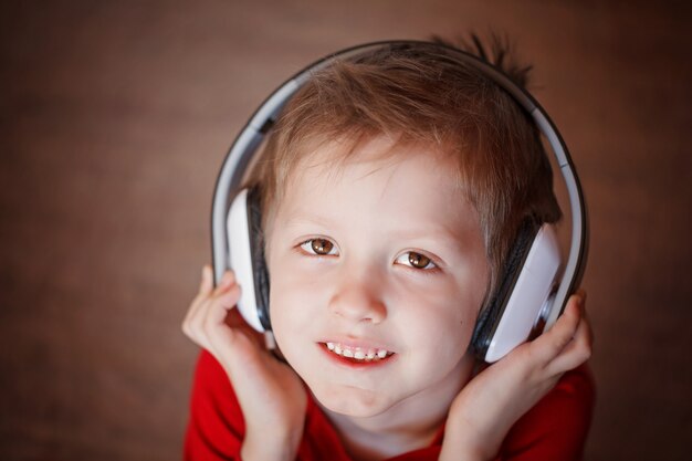 Retrato del primer de un muchacho sonriente que escucha la música en los auriculares.