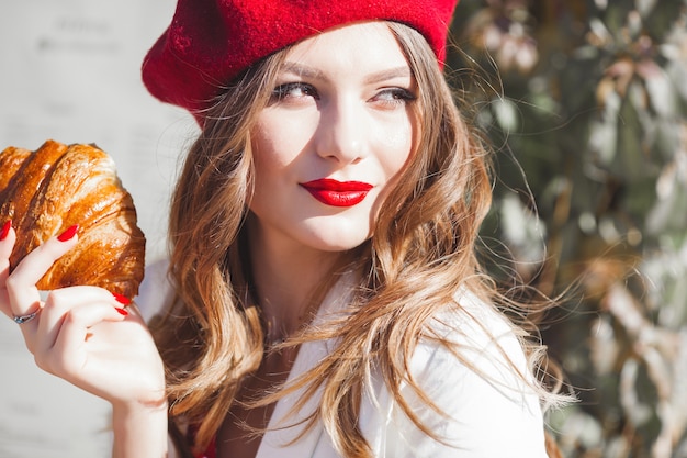 Retrato del primer de la mujer hermosa joven que come el cruasán. Chica francés.