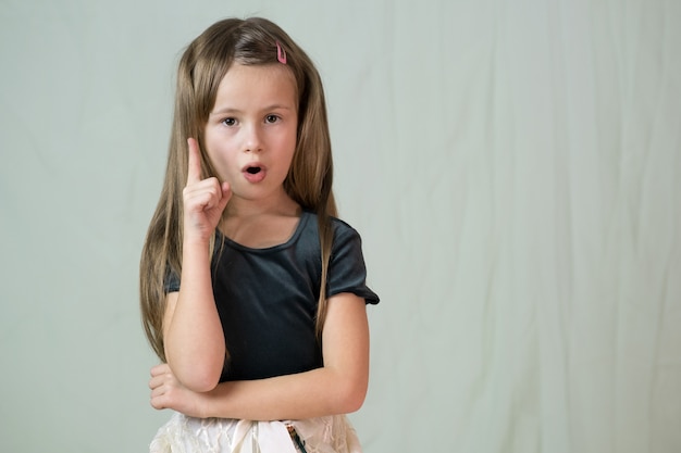 Retrato del primer de la niña sonriente feliz con el pelo largo que detiene su finger que tiene una idea.