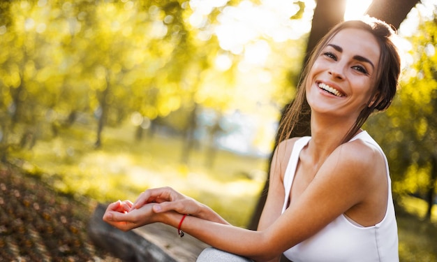 Foto retrato en primer plano de una adorable y hermosa mujer morena con maquillaje y peinado profano posando al aire libre en la puesta de sol con rayos de sol modelo de moda de moda