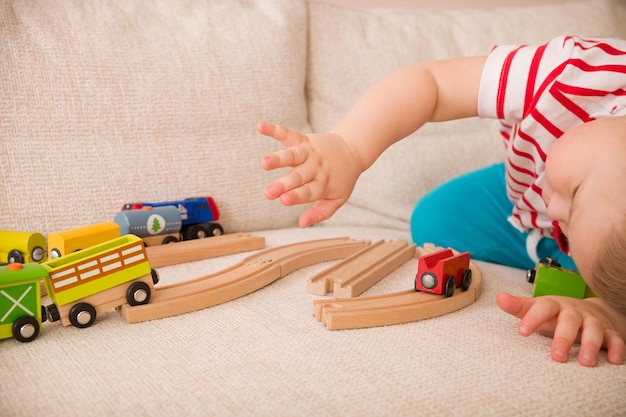 Retrato de primer plano de un adorable niño pequeño jugando con ferrocarriles y trenes coloridos. Concepto de educación