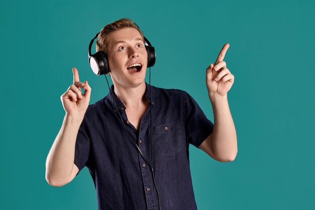 Retrato de primer plano de un apuesto hombre adulto de jengibre con una elegante camiseta azul marino escuchando la música a través de unos auriculares mientras posa en el fondo azul del estudio. Expresiones faciales humanas. emoción sincera