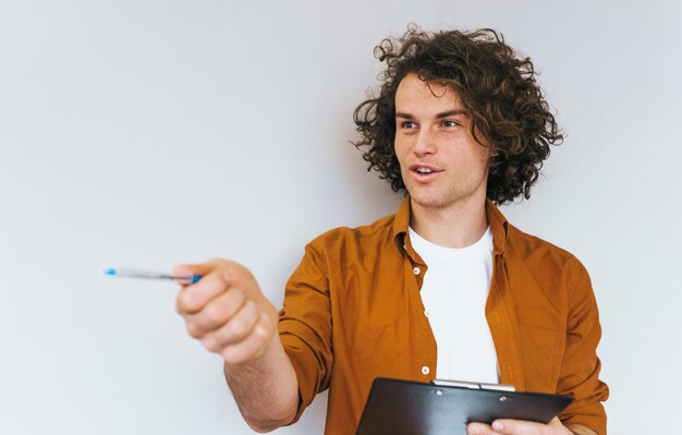 Foto retrato de primer plano de un apuesto hombre de negocios con el pelo rizado pensando en un plan para la próxima semana vistiendo una camiseta blanca y una camisa. el gerente ocupado toma notas en el cuaderno para reservar y enviar pedidos.