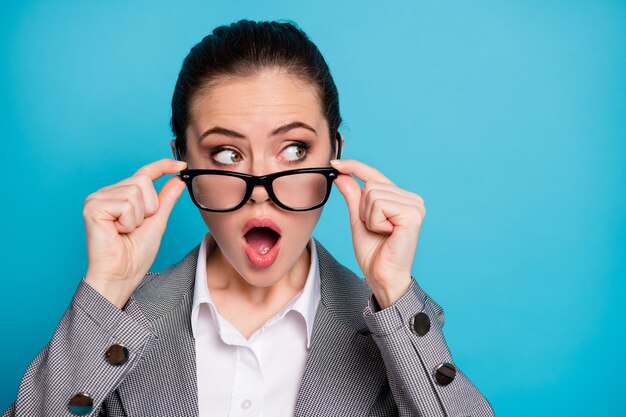 Retrato de primer plano de la atractiva chica asombrada sorprendida mirando a un lado tocando especificaciones aisladas sobre fondo de color azul brillante