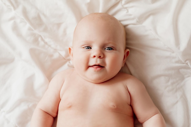 Retrato de primer plano de un bebé recién nacido de ojos azules acostado boca arriba en una sábana blanca feliz despreocupado