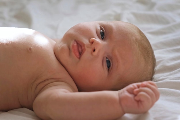 Retrato de primer plano de un bebé recién nacido en una sábana blanca Enfoque suave El bebé está acostado bostezando Una niña de dos semanas de edad Despertándose en la cama en casa Nueva vida y concepto de crecimiento Personas reales