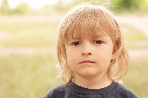 retrato de primer plano de la cara pensativa de un niño rubio en una calle de verano de fondo verde