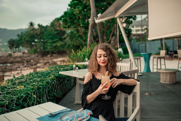 Retrato de primer plano. Chica elegante con peinado rizado divirtiéndose en el bar de verano de lujo.