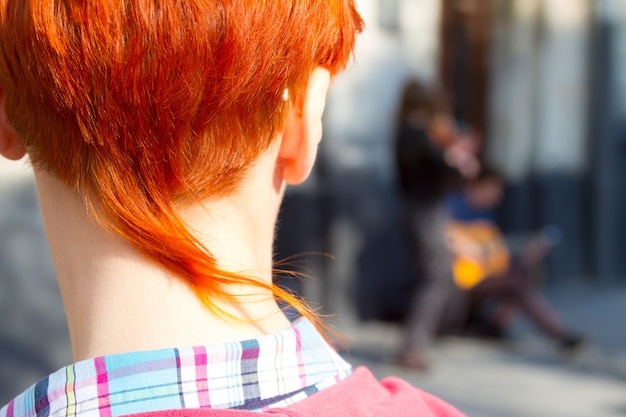 Retrato de primer plano de una chica pelirroja con un elegante corte de pelo mira una actuación de músicos callejeros