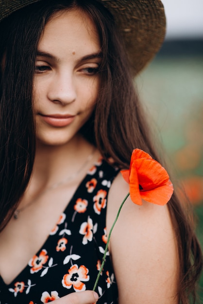 Retrato de primer plano de una hermosa niña libre en un sombrero en un campo de verano de amapolas rojas