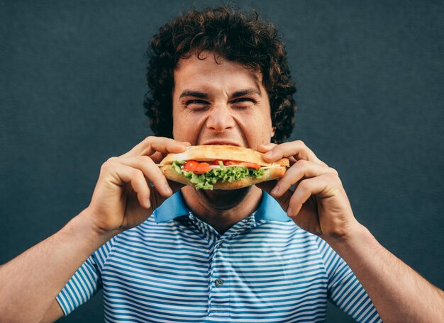 Retrato de primer plano de un hombre guapo joven comiendo una hamburguesa con queso Hombre feliz en un restaurante de comida rápida comiendo una hamburguesa al aire libre Hombre con cabello rizado comiendo comida callejera y comiendo una hamburguesa