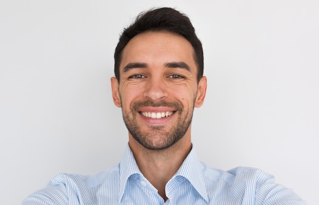 Retrato de primer plano de un hombre joven y guapo feliz sonriendo con una sonrisa dentuda saludable mirando a la cámara haciendo un autorretrato Hombre alegre sin afeitar con camisa azul posando en el fondo del estudio Gente