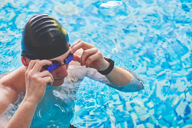 Retrato de primer plano de un hombre musculoso deportivo con gafas de natación y una gorra en una piscina interior