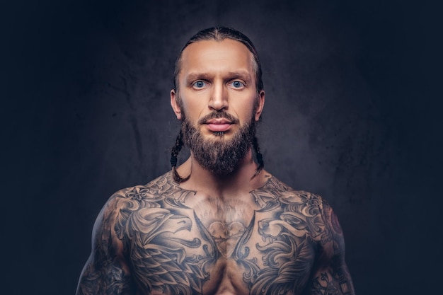 Retrato de primer plano de un hombre musculoso tatuado con barba y un elegante corte de pelo. Aislado en un fondo oscuro.