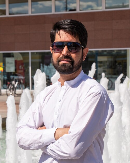 Retrato en primer plano de un hombre paquistaní moderno con barba oscura, ropa ligera y gafas de sol