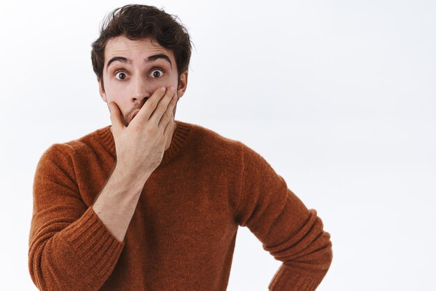 El retrato de primer plano de un hombre sorprendido y asombrado escucha una historia increíble que cubre la boca con la mano y dice wow mirando la cámara con los ojos abiertos mientras escucha una historia impresionante e interesante de fondo blanco.