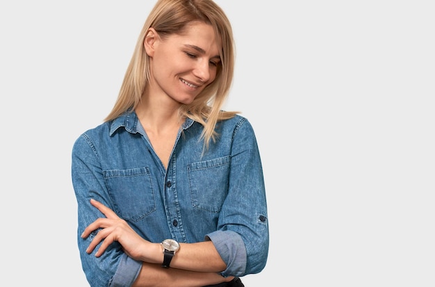 Retrato de primer plano horizontal de una mujer de negocios bastante sonriente con cabello rubio con camisa de mezclilla sobre fondo blanco Mujer caucásica feliz posando en la pared del estudio con espacio de copia para su promoción