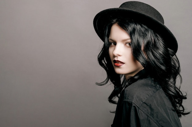 Retrato de primer plano de joven belleza modelo de moda mujer con sombrero en una pared gris, labios rojos