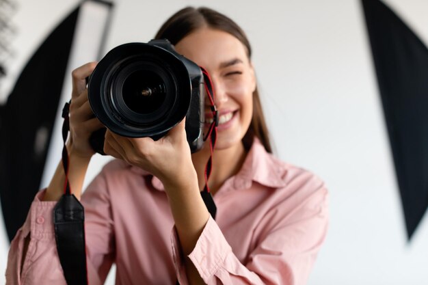 Retrato de primer plano de una joven fotógrafa que toma una foto de una dama que trabaja en un estudio fotográfico con equipo de iluminación