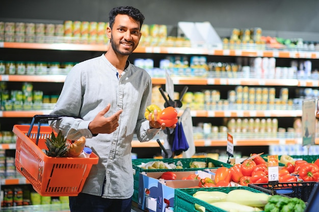 Retrato en primer plano de un joven guapo recogiendo pimientos escogiendo verduras amarillas y naranjas en la tienda de comestibles