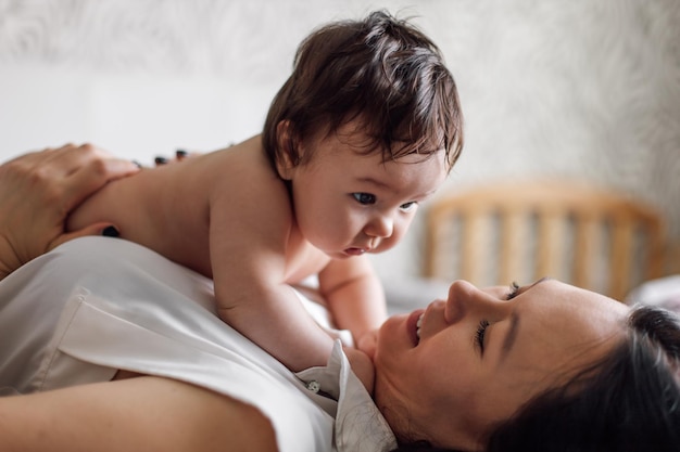 Retrato de primer plano de la joven madre feliz y el bebé acostados en la cama en la habitación Sostenga con cuidado al bebé desnudo en brazos sobre el pecho Espacio de copia libre de enfoque selectivo Concepto de afecto materno y cuidado de niños