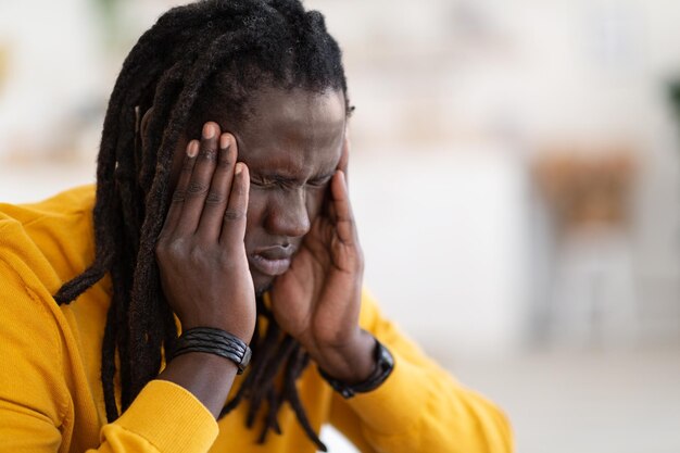 Retrato de primer plano de un joven negro enfermo que sufre de dolor de cabeza en casa