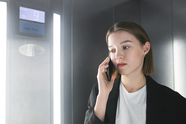 Retrato de primer plano de una joven oficinista hablando por su teléfono en el ascensor.