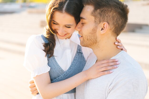 Retrato de primer plano de la joven pareja amorosa descansando en el parque de la ciudad sentado abrazando en un banco en un día soleado de verano. Relaciones feliz novio y novia disfrutando de pasar tiempo juntos al aire libre.