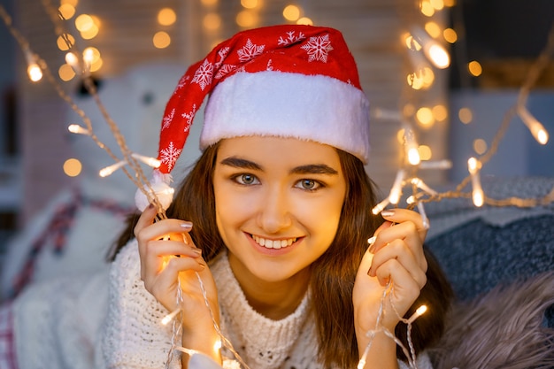 Retrato de primer plano de una linda joven riendo con un sombrero de Santa en la cabeza con guirnaldas en sus manos