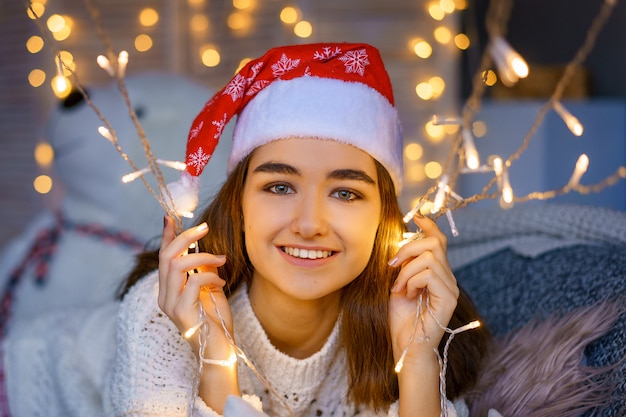 Retrato de primer plano de una linda joven riendo con un sombrero de Santa en la cabeza con guirnaldas en sus manos