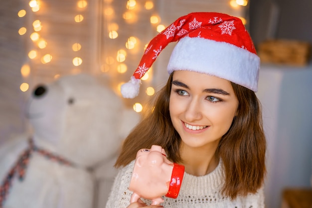 Retrato de primer plano de una linda joven riendo con un sombrero de Santa en la cabeza con guirnaldas en sus manos