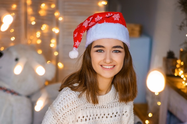 Retrato de primer plano de una linda joven riendo con un sombrero de Santa en la cabeza con guirnaldas en sus manos