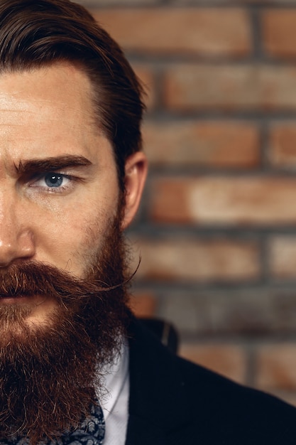 Foto retrato de primer plano de media cara de un hombre serio con bigote y barba con traje. en el contexto de una pared de ladrillos.