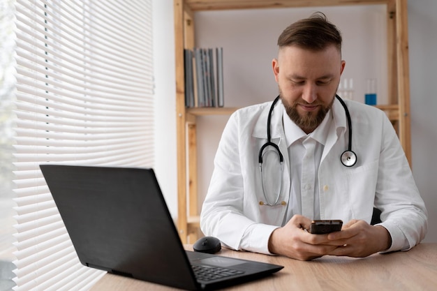 Foto retrato en primer plano de un médico que utiliza un teléfono inteligente móvil trabaja en una computadora portátil en una oficina médica en un sistema de registro médico electrónico ehr de un hospital