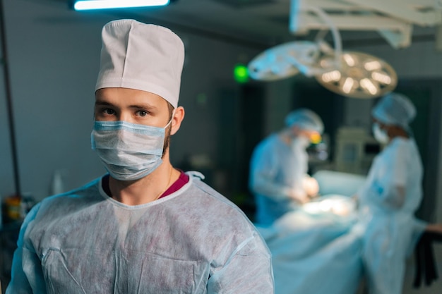 Retrato en primer plano de un médico en uniformes quirúrgicos y máscaras de pie posando mirando a la cámara en